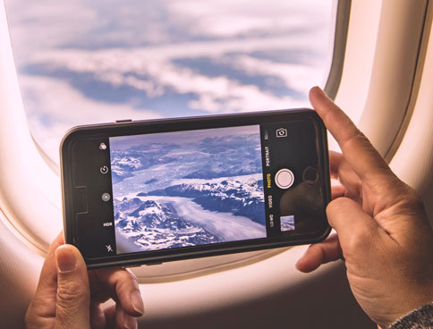 man taking photos of mountains on a smartphone out of plane window